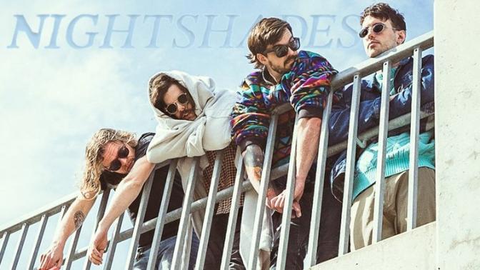 4 men casually dressed wearing sunglasses hanging over a railing