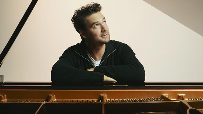 Pianist Michael Kaeshammer seated at a piano looking skyward