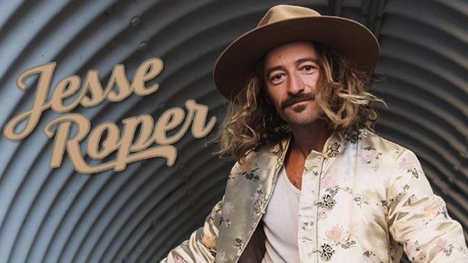 musiciaan Jesse Roper inside a metal culvert wearing a light brown hat, white tank top and embroidered cream colored jacket