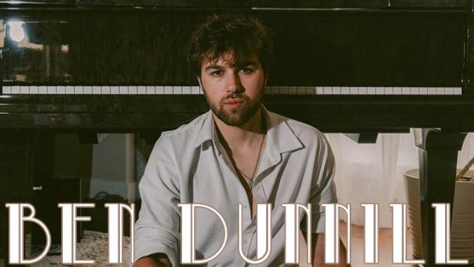 Musician Ben Dunnill seated on the ground in front of a piano 