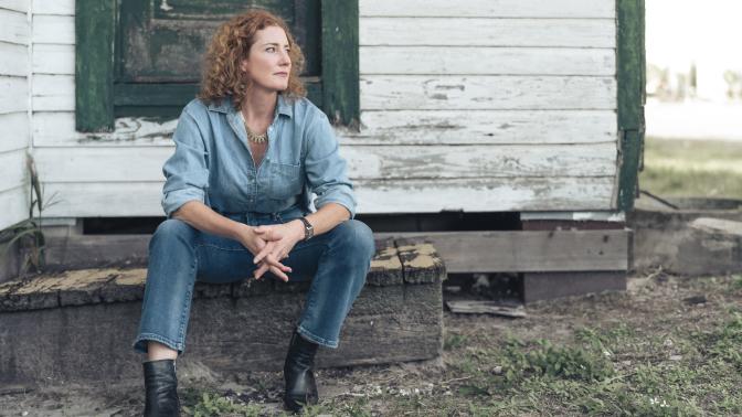 Musician Kathleen Edwards seated in front of a rustic white and green home dressed in denim