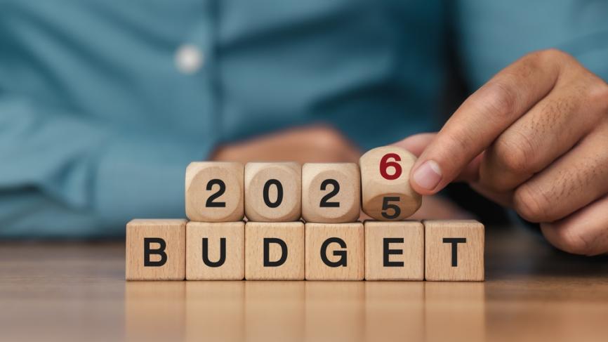 a man's fingers spelling out 2026 budget with wooden blocks