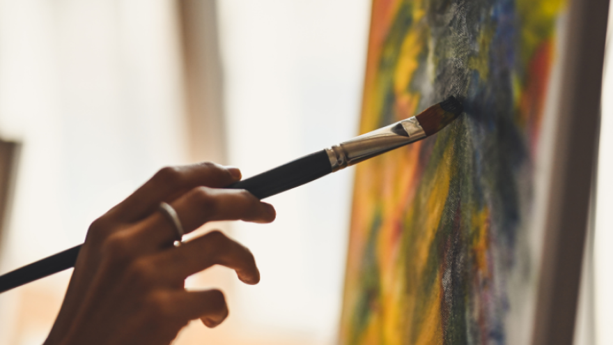 Persons hand holds a paintbrush against a canvas 