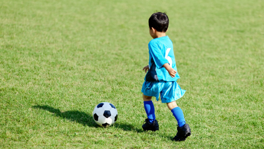 A young child chasing after a soccer ball outside