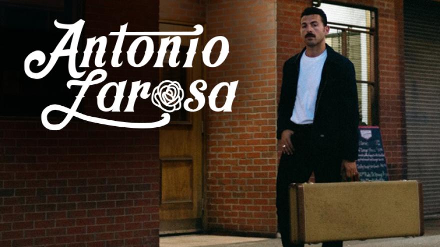 Antonio Larosa walking down a street carrying a vintage guitar case at night