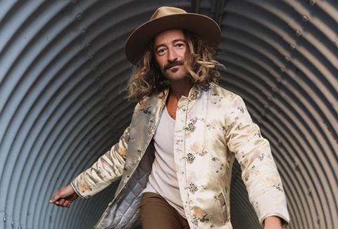 musical artist jesse roper runningthrougha culvert wearing an embroidered cream coat and tan colored hat