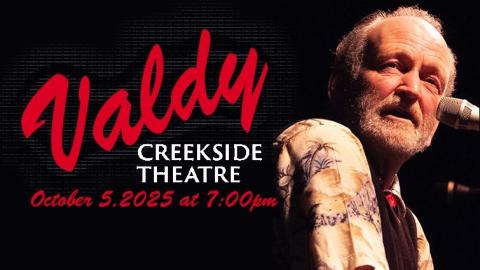 musician Valdy turns his face sideways as he sings into a microphone under a spotlight