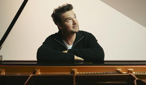 Pianist Michael Kaeshammer seated at a piano looking skyward