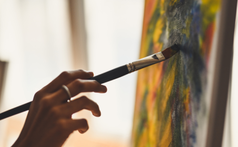 Persons hand holds a paintbrush against a canvas