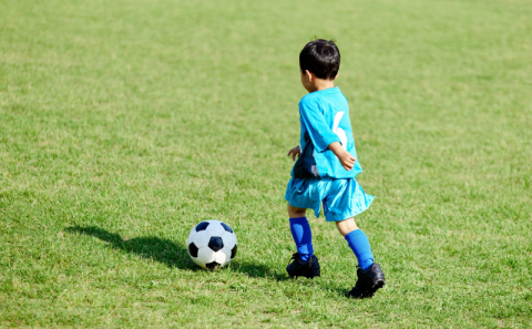 A young child chasing after a soccer ball outside