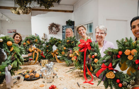 5 women around a table holding winter wreaths