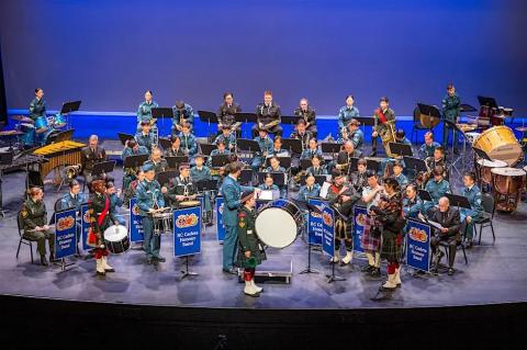 seated orchestra of musicians that are all cadets in their cadet uniforms with various instruments