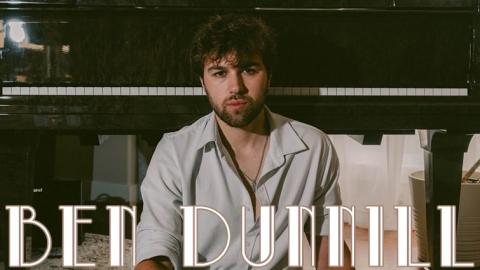 Musician Ben Dunnill seated on the ground in front of a piano