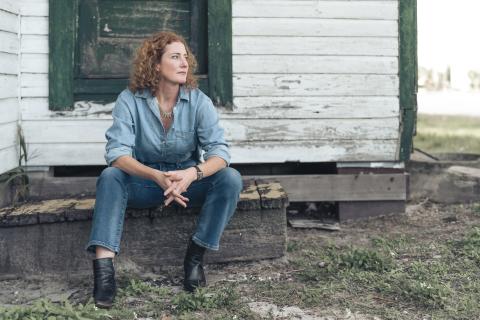 Musician Kathleen Edwards seated in front of a rustic white and green home dressed in denim
