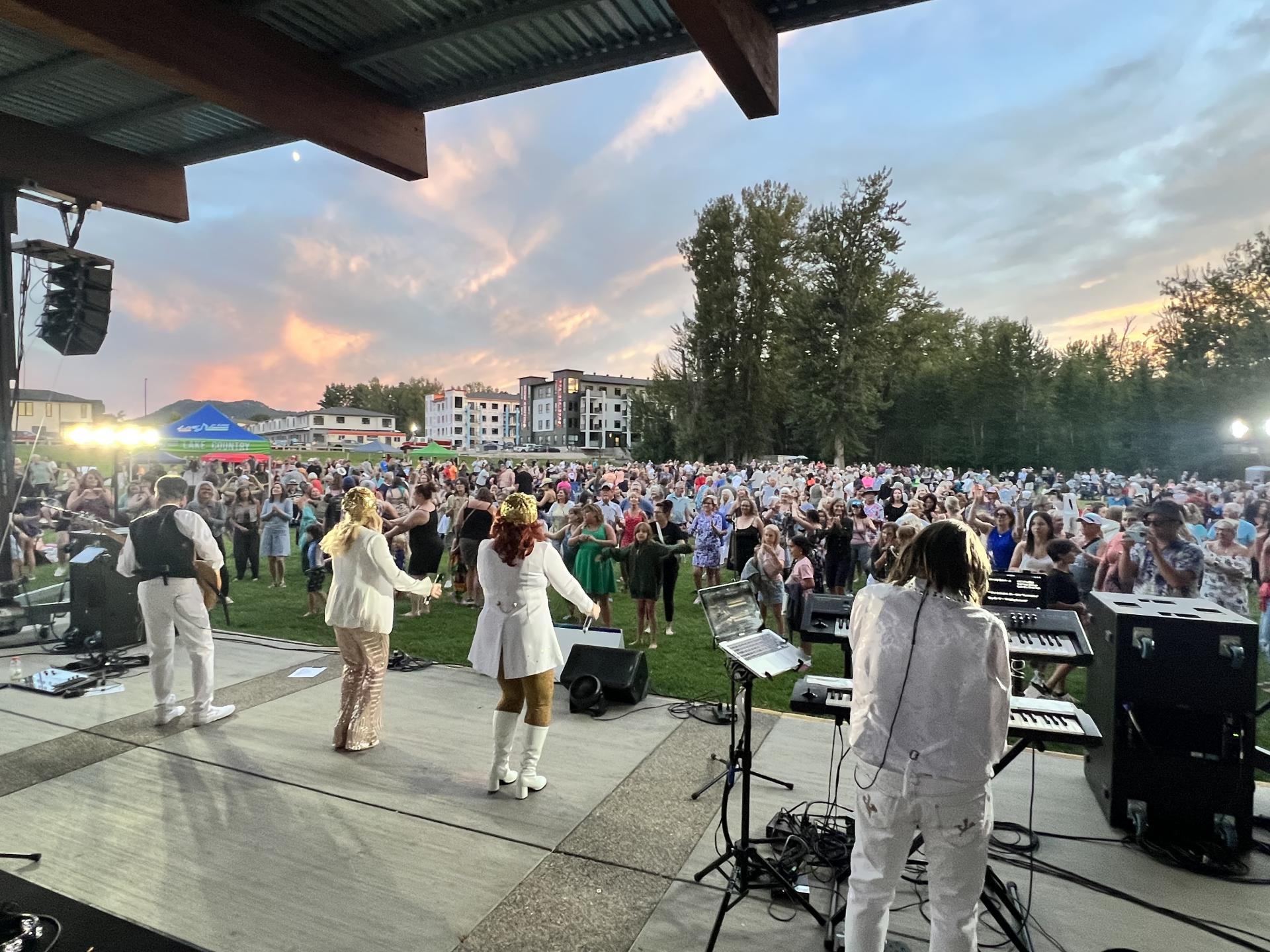 ABBA tribute band performing in front of a large crowd at a park